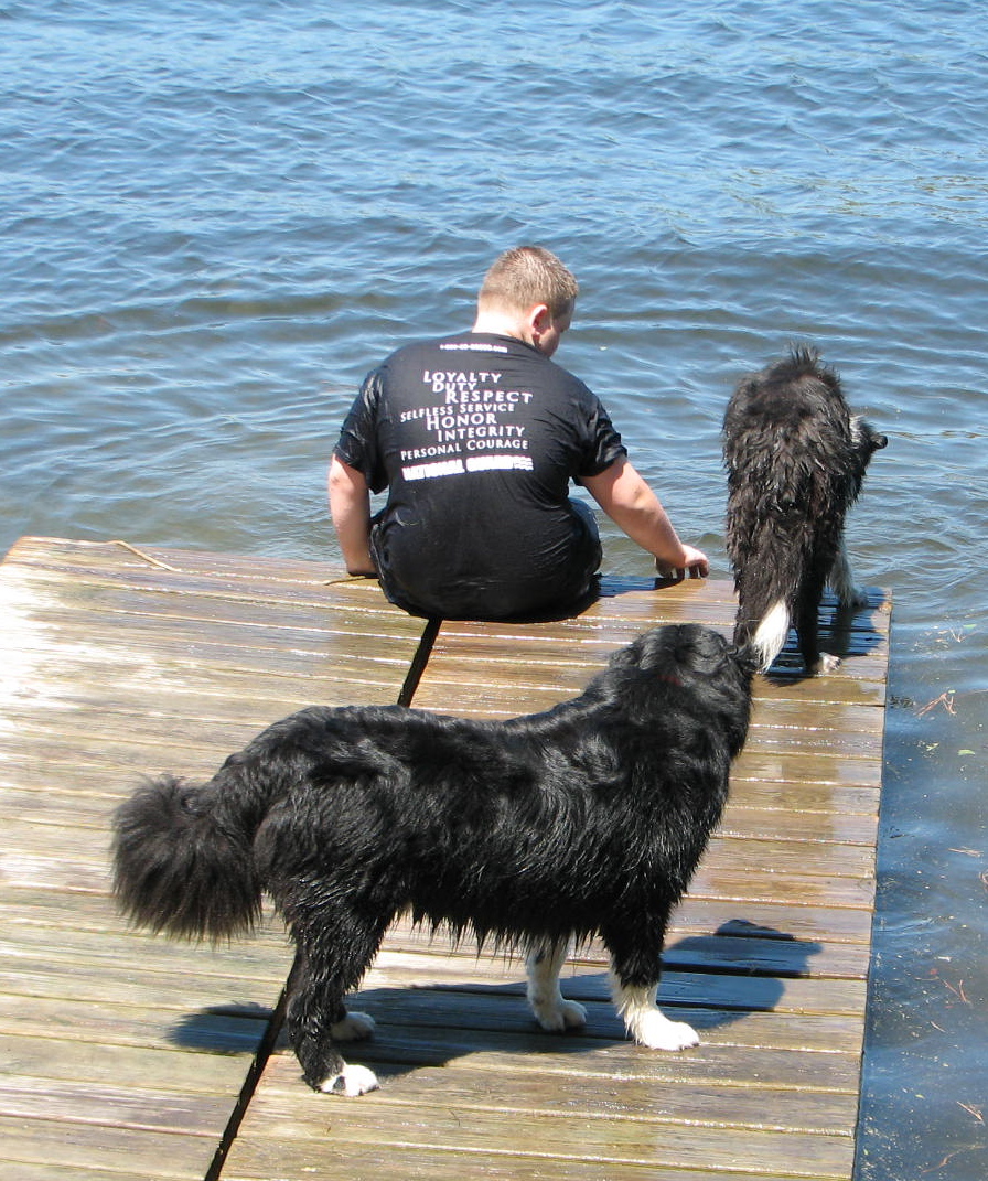 boy sitting on pier with 2 dogs looking at the water